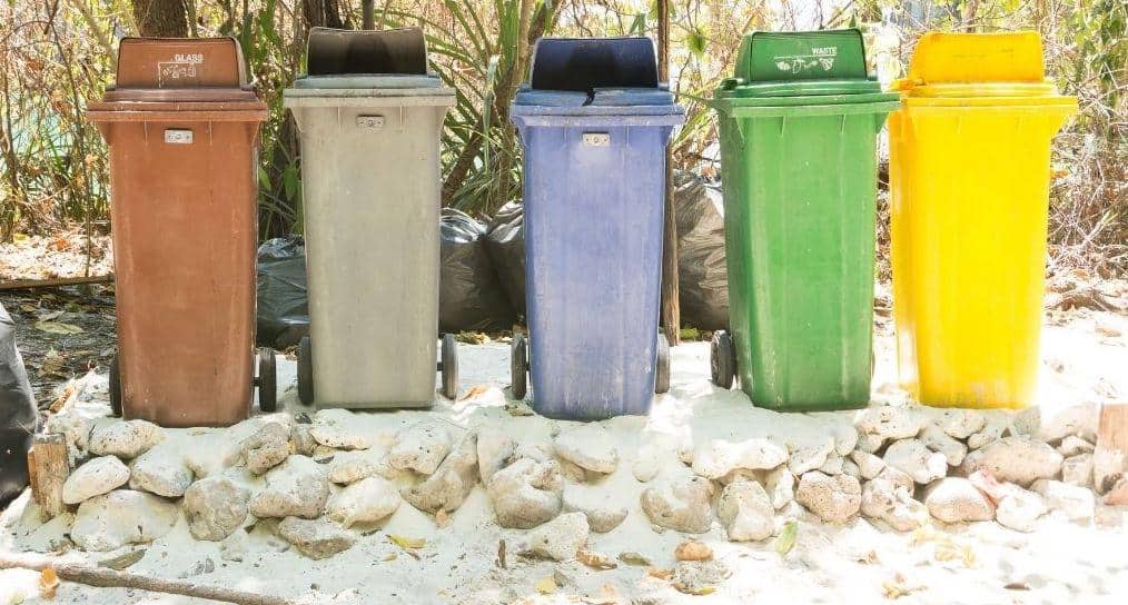 A colorful assortment of designated trash receptacles on a stone wall at a campsite ranging from yellow and bright green to blue and neutrals. 