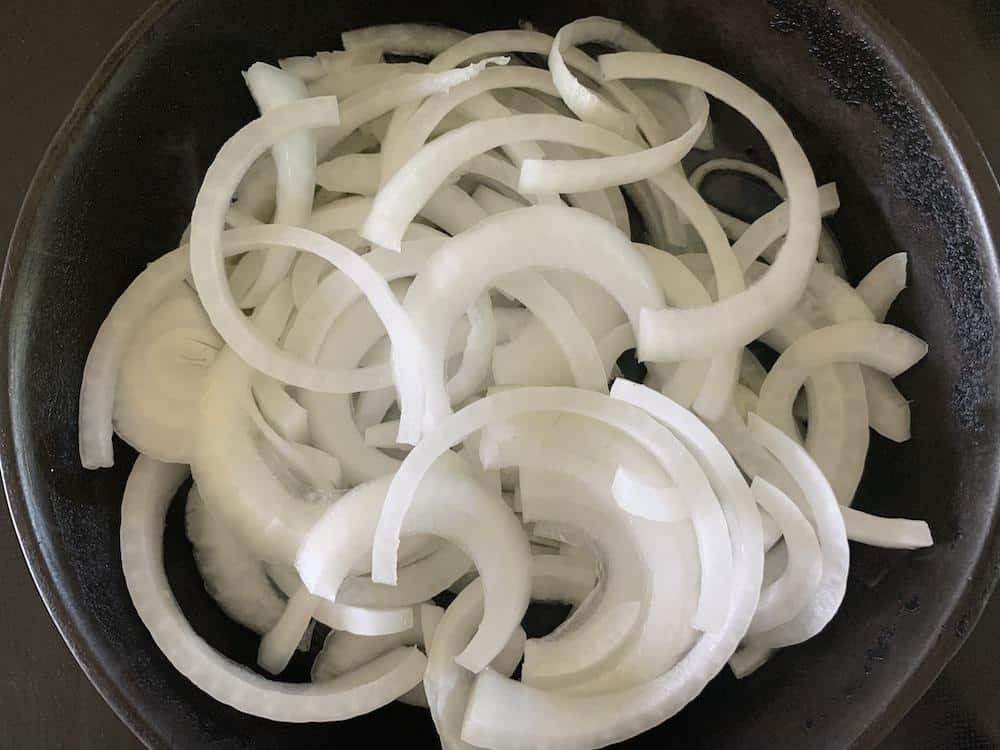 Thinly sliced onions in a cast iron pan await caramelization.