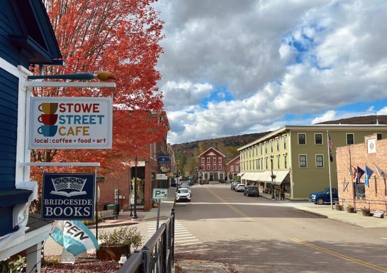 Downtown Waterbury is cheery on a fall day with a vibrant red maple, sunshine and partly cloudy skies above the Stowe Street Cafe sign.