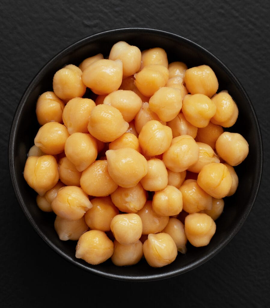 A close up from above of canned chickpeas in a black bowl on a black counter.