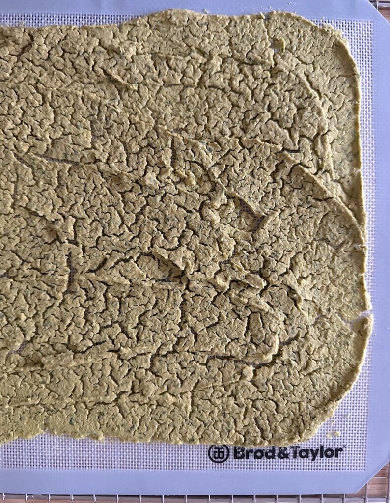 A close up of dehydrated hummus that is crumbly and on a white drying mat.