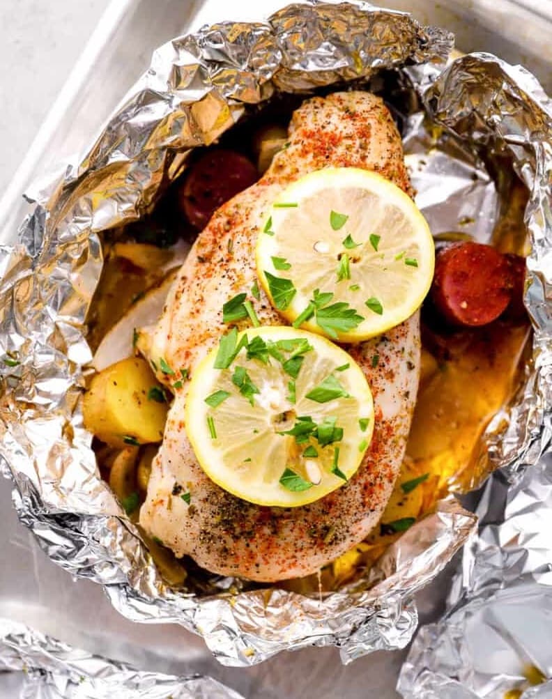 Baked lemon chicken sits in a foil packet with potatoes and veggies ready for grilling.
