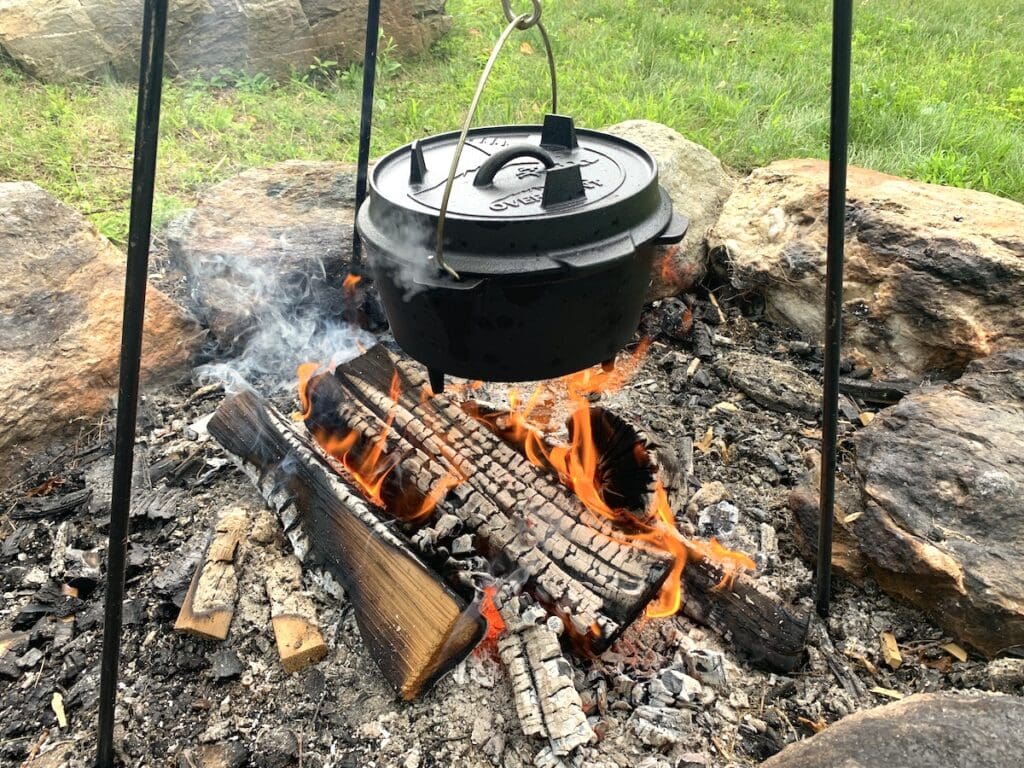 A Dutch oven is hung on a tripod over a campfire to cook up all the camping food ideas for a family!