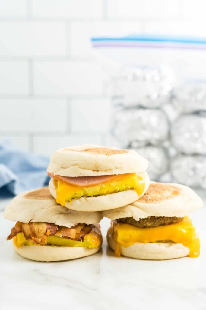 A stack of breakfast sandwiches with different fillings: ham, sausage, and bacon — these are perfect to freeze and then thaw for camping breakfasts!