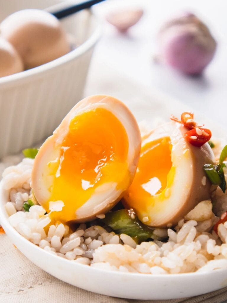 Korean marinated eggs ooze soft boiled yolk onto a bowl of rice when sliced open.