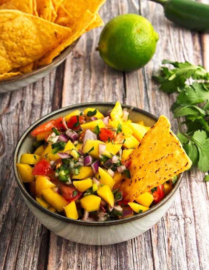 Mango salsa is in a bowl with a tortilla chip ready for munching on!