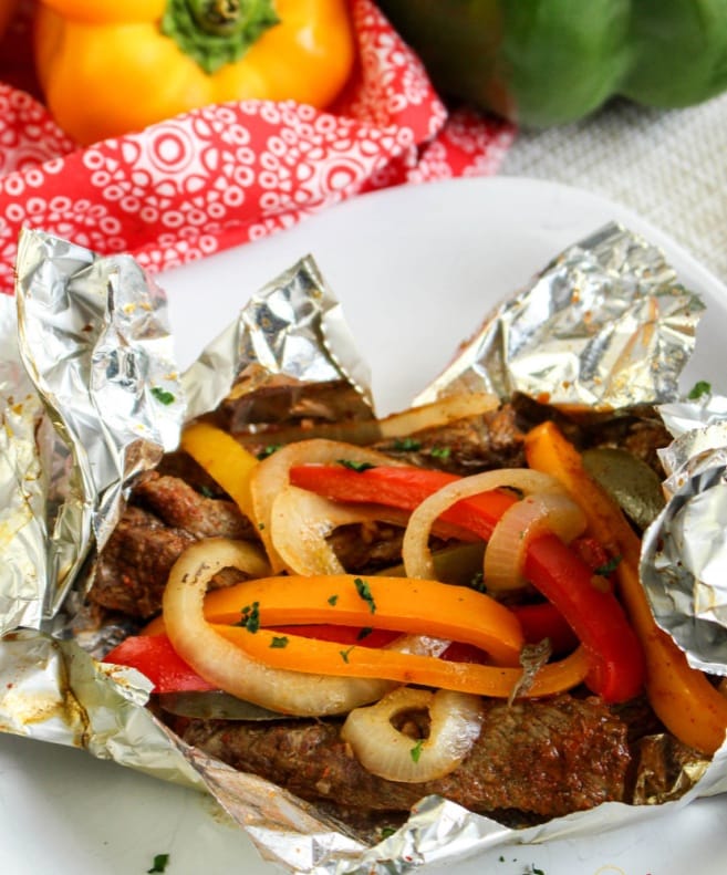 Steak fajitas are served up in foil packets with orange and red sweet peppers and onions.