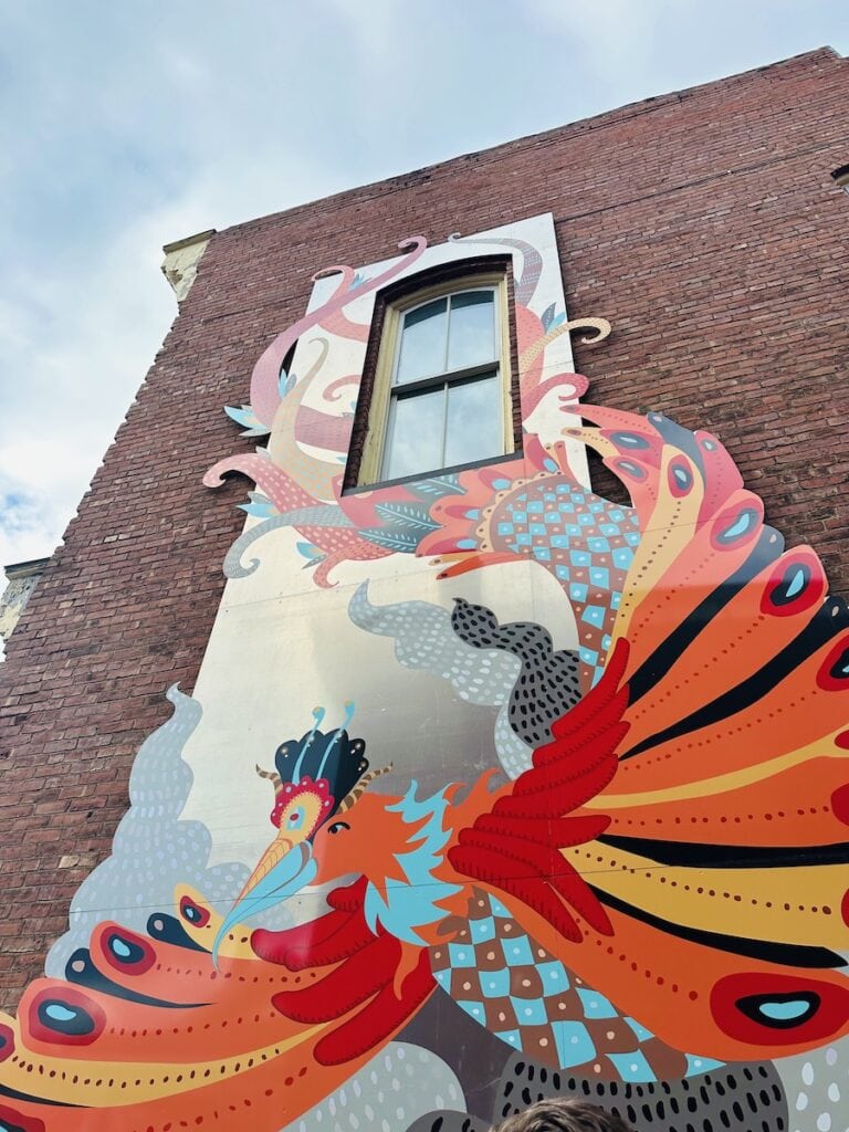 Phoenix Rising, art located in the alley across the street from Axel's Gallery & Frame Shop is vibrantly colored with oranges, reds, and blues