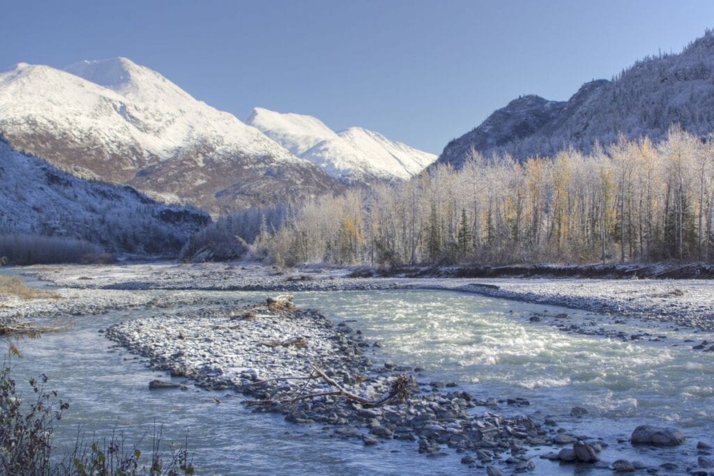 The Tsina River, located on the northern end of Thompson Pass, sparkles in the wintery weather of Alaska in November. Glowing snow-kissed mountains tower in the background in the sunlight.