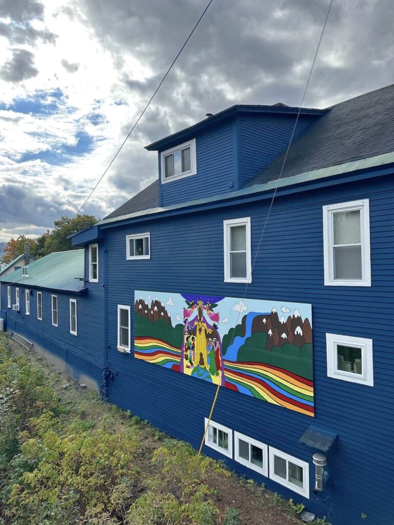 Madonna's Earth is a beautiful elongated mural with all the colors of the rainbow depicting mountains and a river with loving people welcoming all.