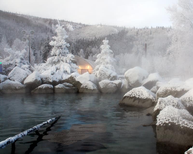 The hot springs water creates steam above the rocky pool with a snowy and frosty landscape at Chena Hot Springs in the background.