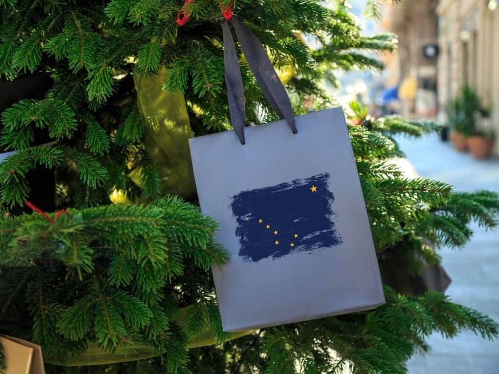 An Alaska state flag is printed on the front of this bag that hangs on a Christmas teee.