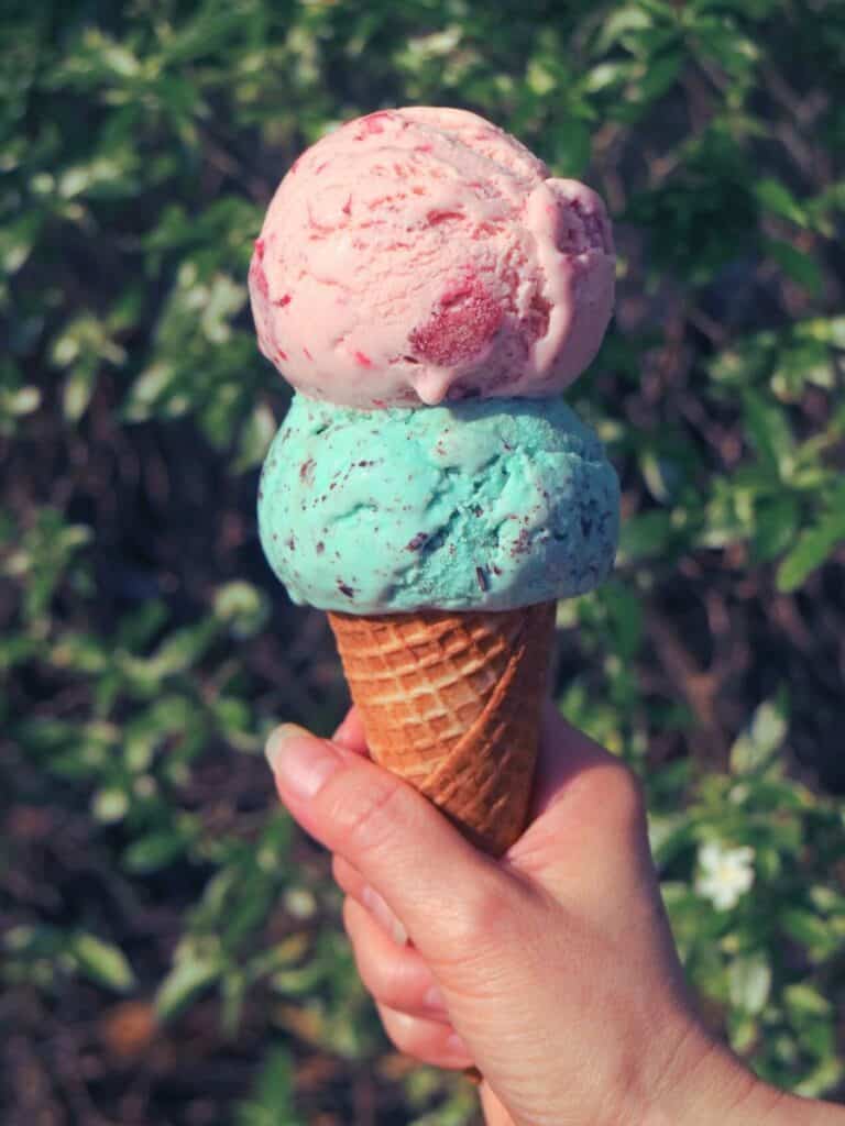 Pink strawberry ice cream tops mint chocolate chip on and ice cream cone.
