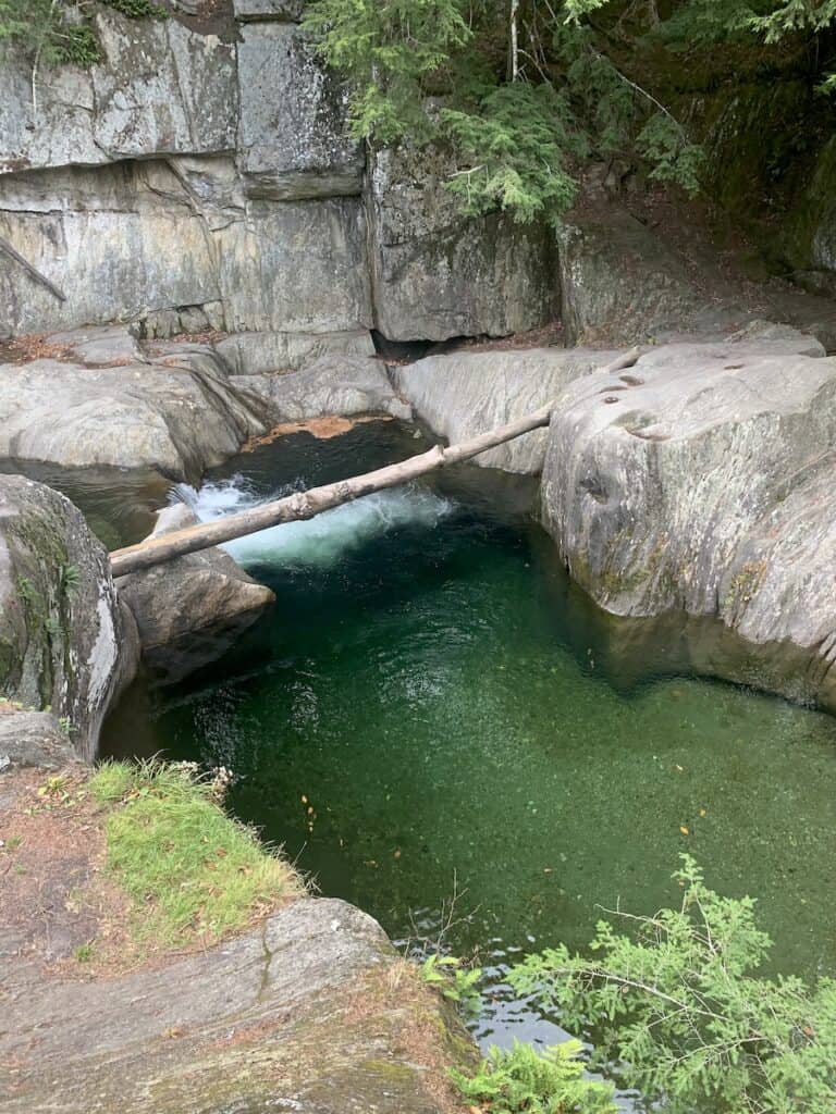 Warren Falls in Vermont is a gorgeous shade of blue-green and is surrounded by granite boulders. A dead log connects two boulders and acts as a footbridge.