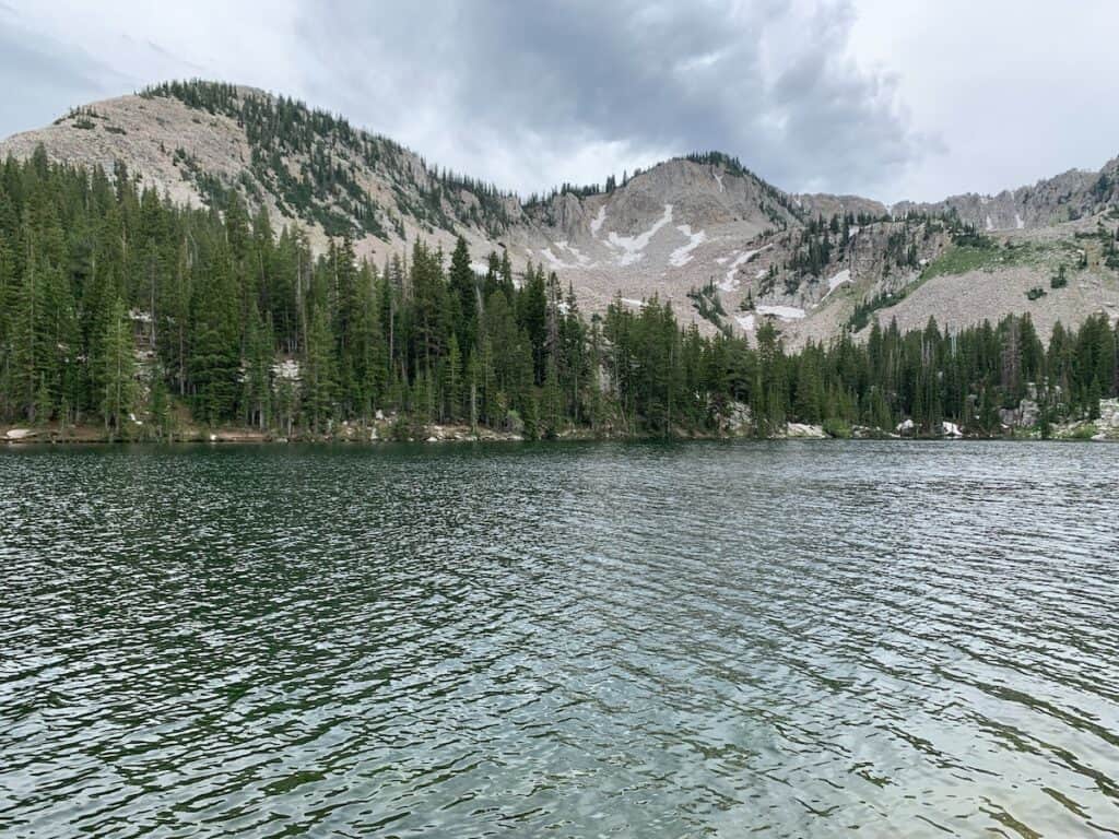 Twin Lakes pristine water ripples in the breeze and the gray rounded mountains and evergreens tower in the backdrop on a cloudy day. 