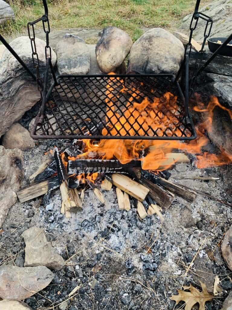 The campfire has been burning for about 30 minutes so the wood has burned down into embers and charcoal, perfect for cooking atop the hanging griddle. The fire pit circle is made with large stones. 
