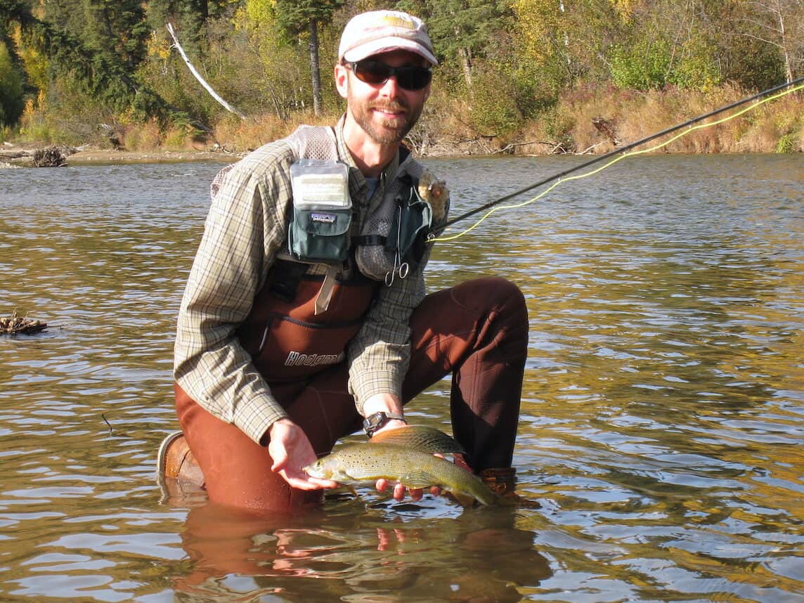This is my husband, Matt showing his grayling catch as he kneels in the river in Alaska.
