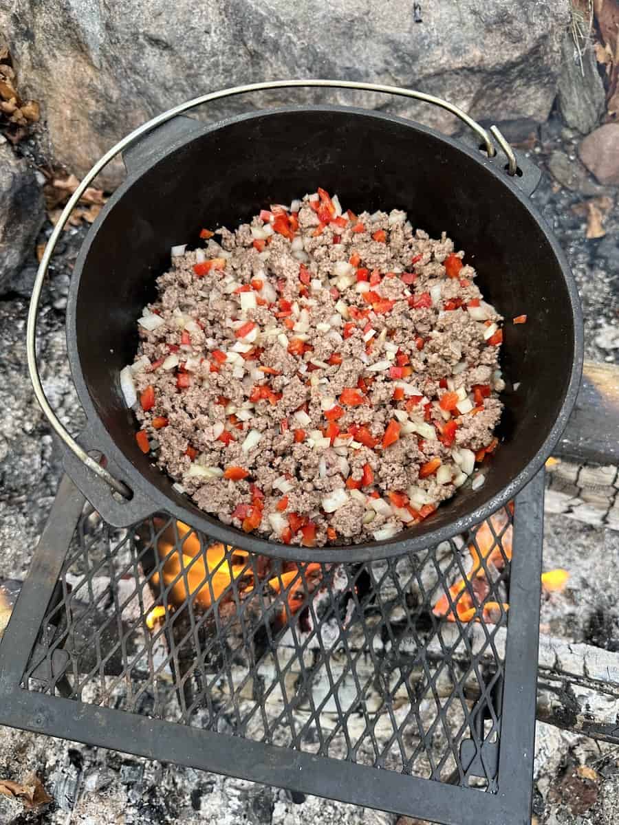 The browned ground beef is in the Dutch oven over the campfire. Chopped ...